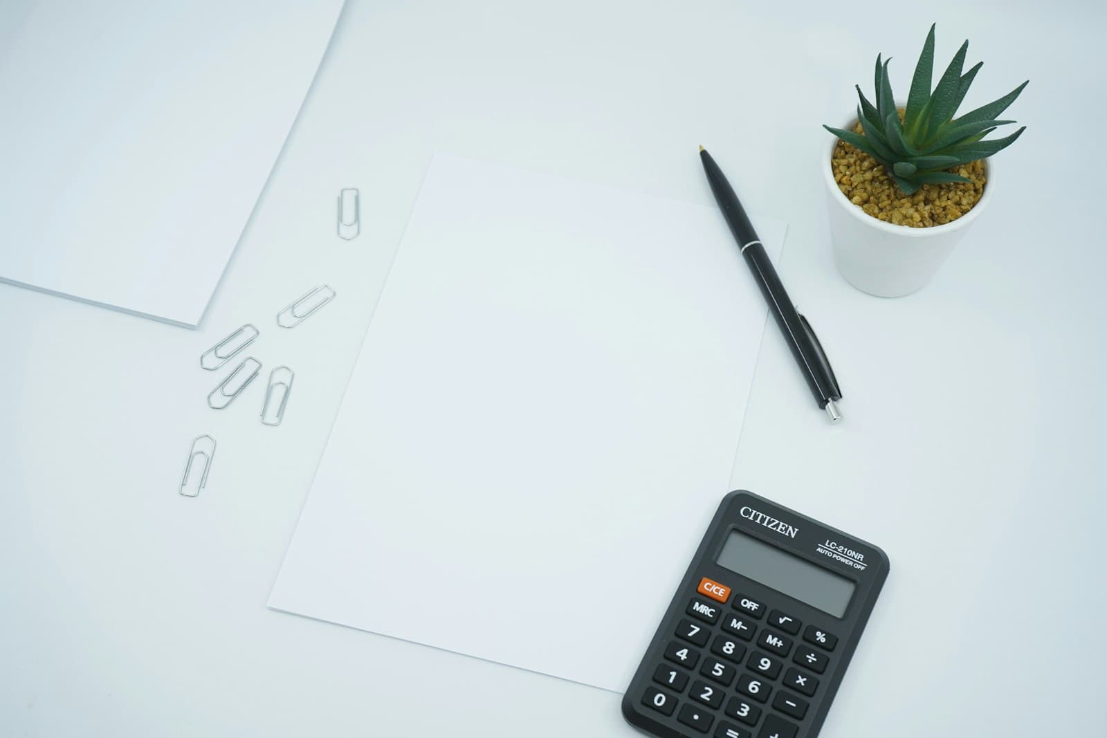 A calculator, pen, blank paper, and paper clips on a clean white desk, illustrating the cost of doing business in Mexico in 2026