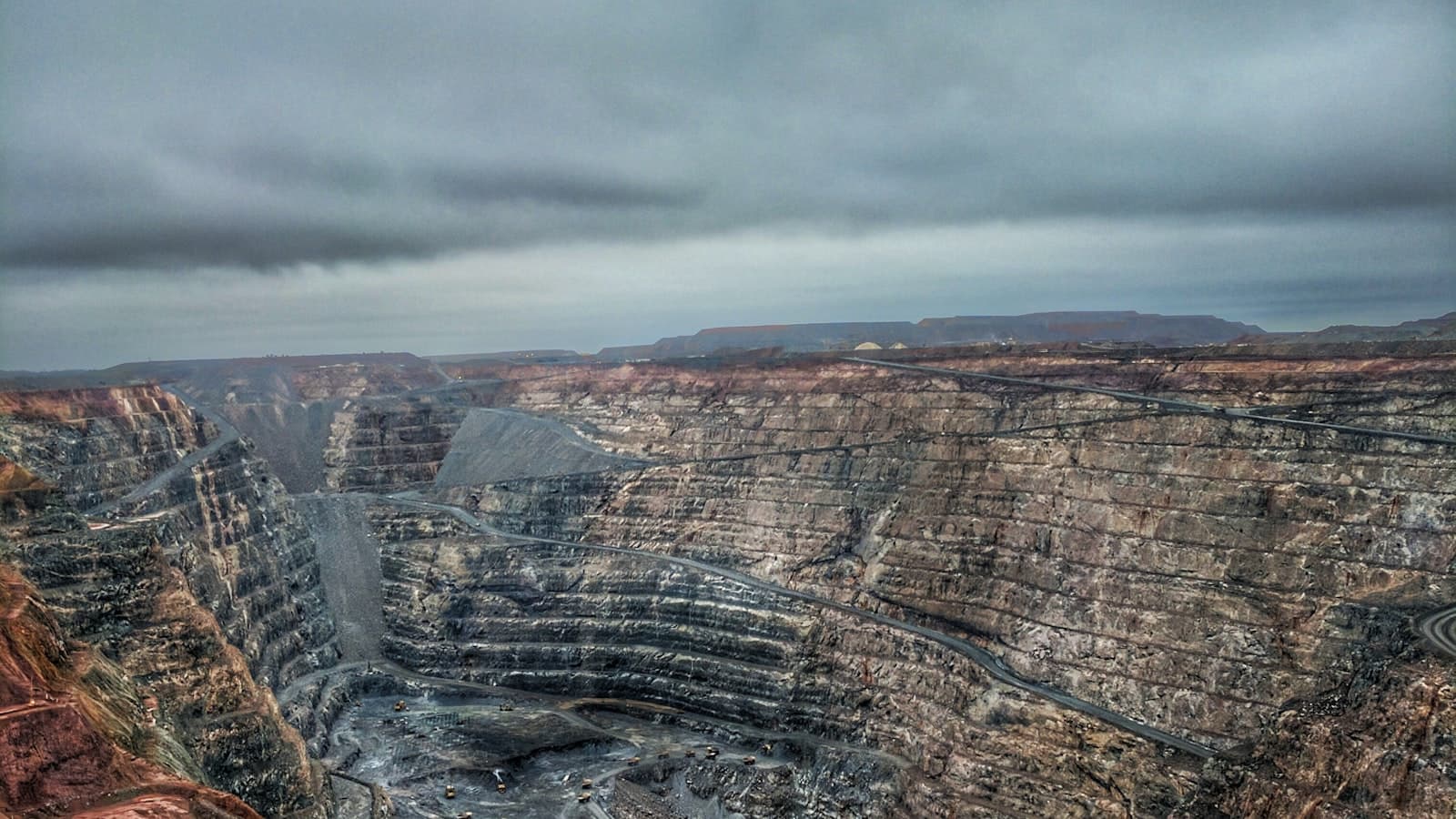 Aerial view of a large terraced open-pit copper mine with haul roads cut into the mineral strata, evoking Mexico's Sonora mining region in the critical minerals corridor