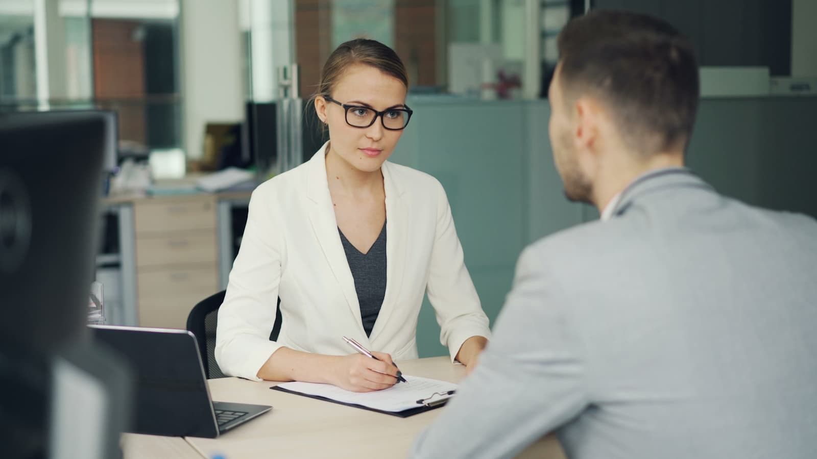 A hiring manager interviewing a job candidate across a desk in a professional office, illustrating the recruiting process behind a company's first hire in Mexico