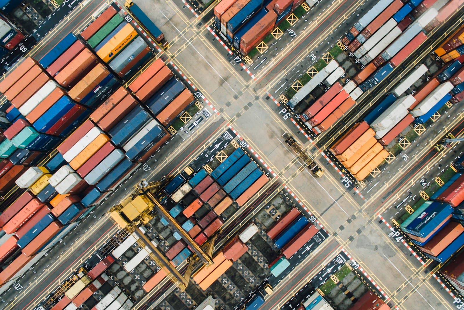Aerial top-down view of a container yard, rows of stacked shipping containers arranged in a grid like classified import categories at a Mexican port