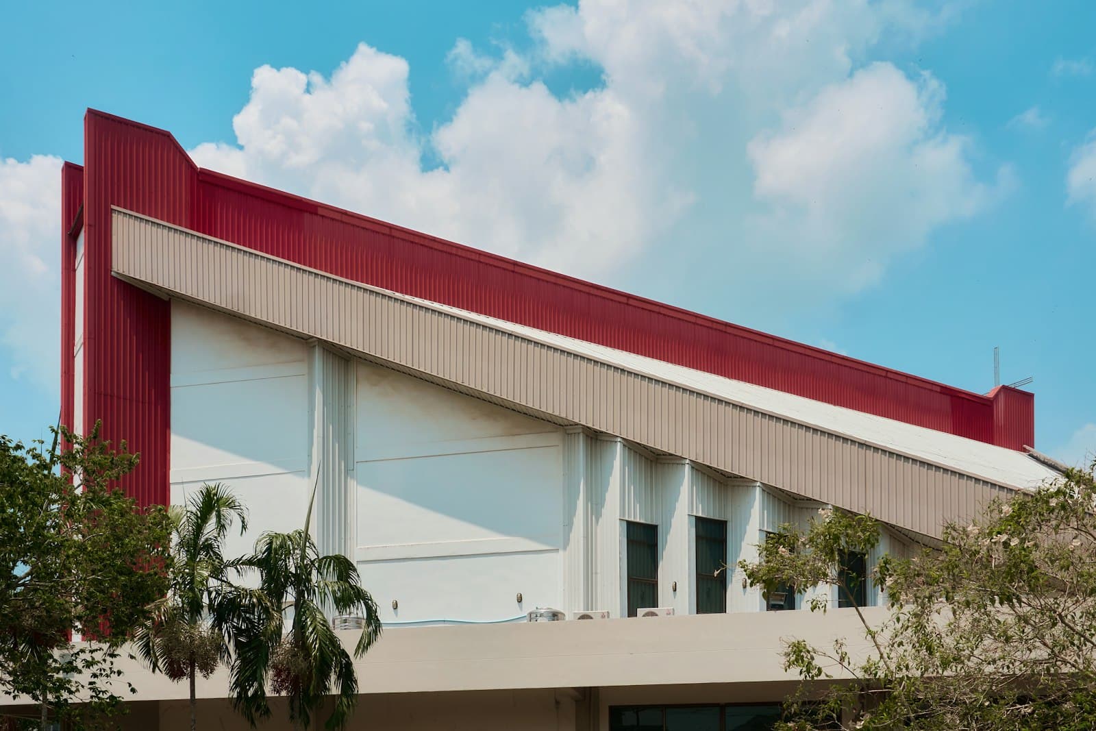 Exterior of a modern manufacturing building with red metal cladding and palm trees under a warm blue sky, evoking an industrial park in northern Mexico