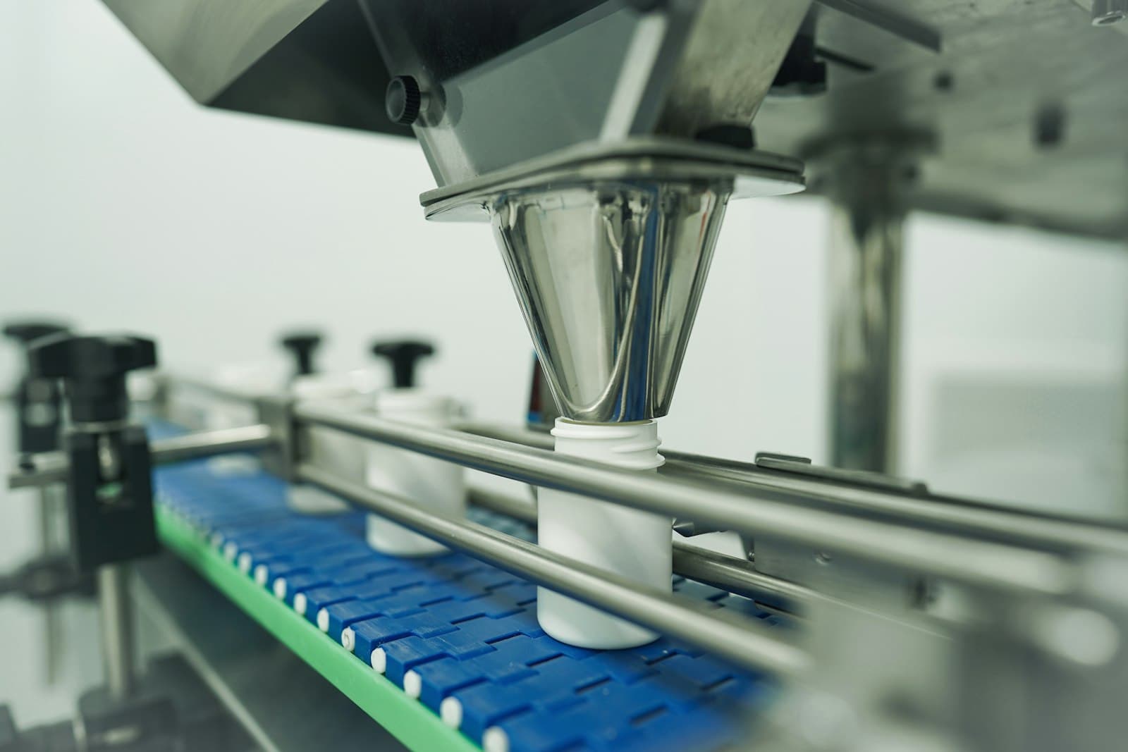 Pharmaceutical filling line dosing white bottles on a blue conveyor inside a clean production facility, the kind of COFEPRIS-regulated manufacturing category affected by Mexico's reform