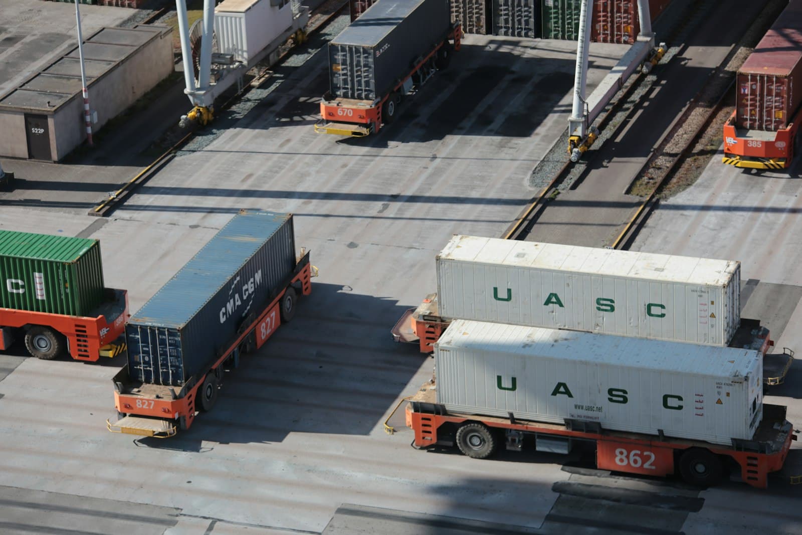 Terminal tractors moving loaded shipping containers beneath gantry cranes at a container port, the point where declared customs value meets the goods themselves