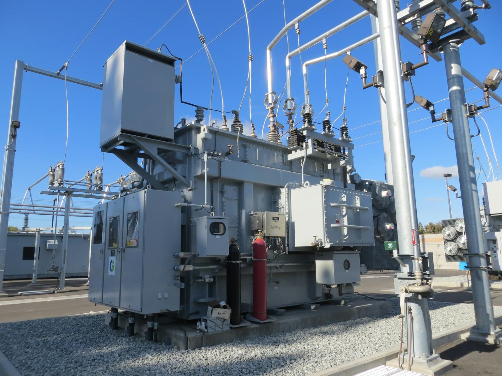 A high-voltage power transformer and switchgear in an electrical substation under a clear sky, the kind of grid capacity that sets the start date of a new manufacturing plant
