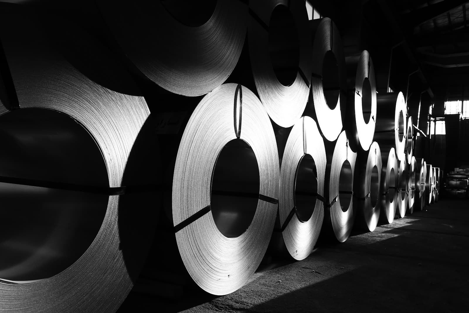Rows of tightly wound steel coils stored in an industrial warehouse, evoking the steel, aluminum, and copper content at the center of the June 2026 Section 232 tariff threshold for cross-border operators supplying the Mexico corridor