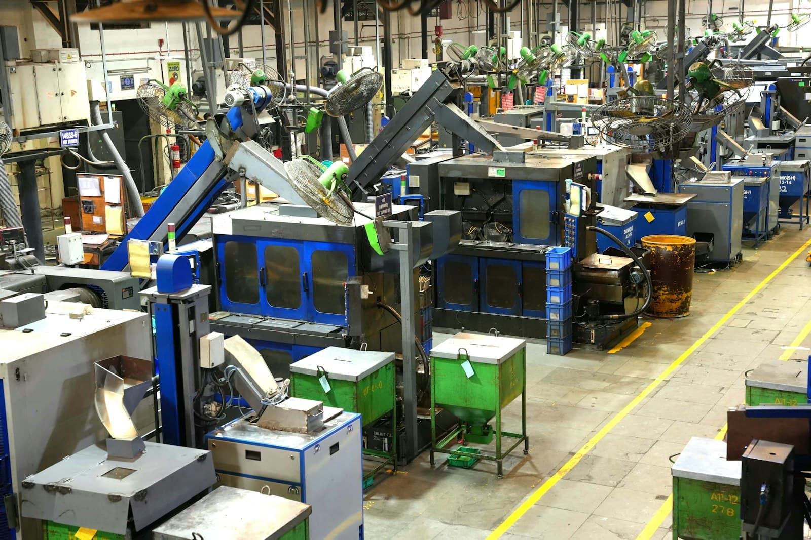 Factory floor lined with blue production machines, green parts bins and yellow aisle markings, the type of export operation that can run as a shelter, a maquiladora or under contract