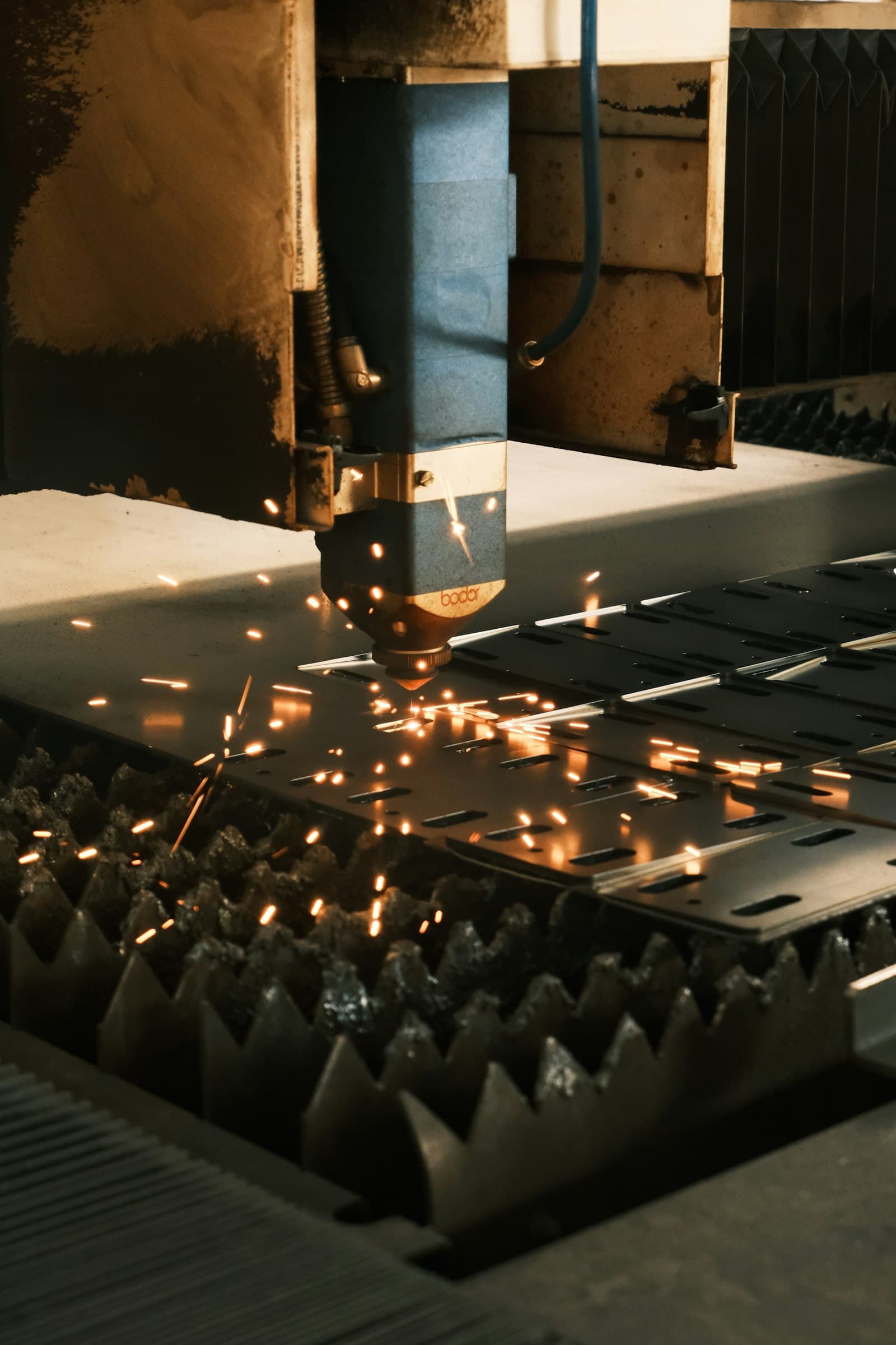 A fiber laser cutting head slicing a sheet of steel on a factory bed, sparks flying, the kind of precision metalwork whose rules-of-origin content is reviewed each year under USMCA through 2036