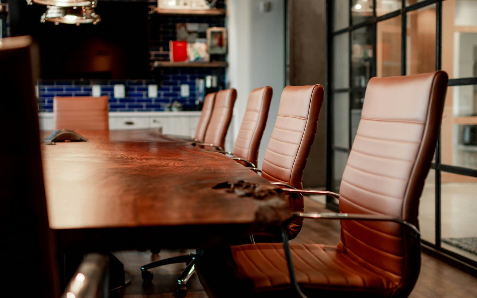 An empty executive boardroom with a long live-edge wooden negotiating table and tan leather chairs, evoking the bilateral USMCA review rounds held in Mexico City