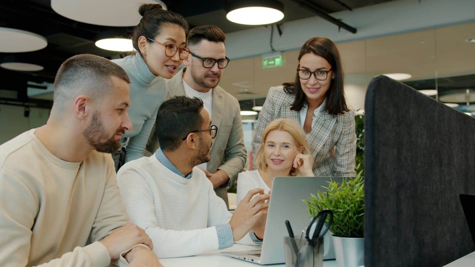 Un equipo internacional reunido frente a una laptop en una oficina moderna, el tipo de equipo mixto que definen la regla del 90 por ciento y el trámite de visas de trabajo en México