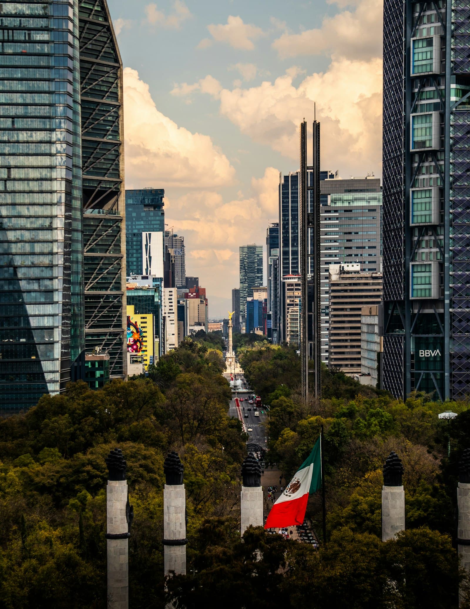 The Mexico City skyline of high-rise office towers rising behind a large Mexican national flag, evoking the country's macroeconomic and investment backdrop